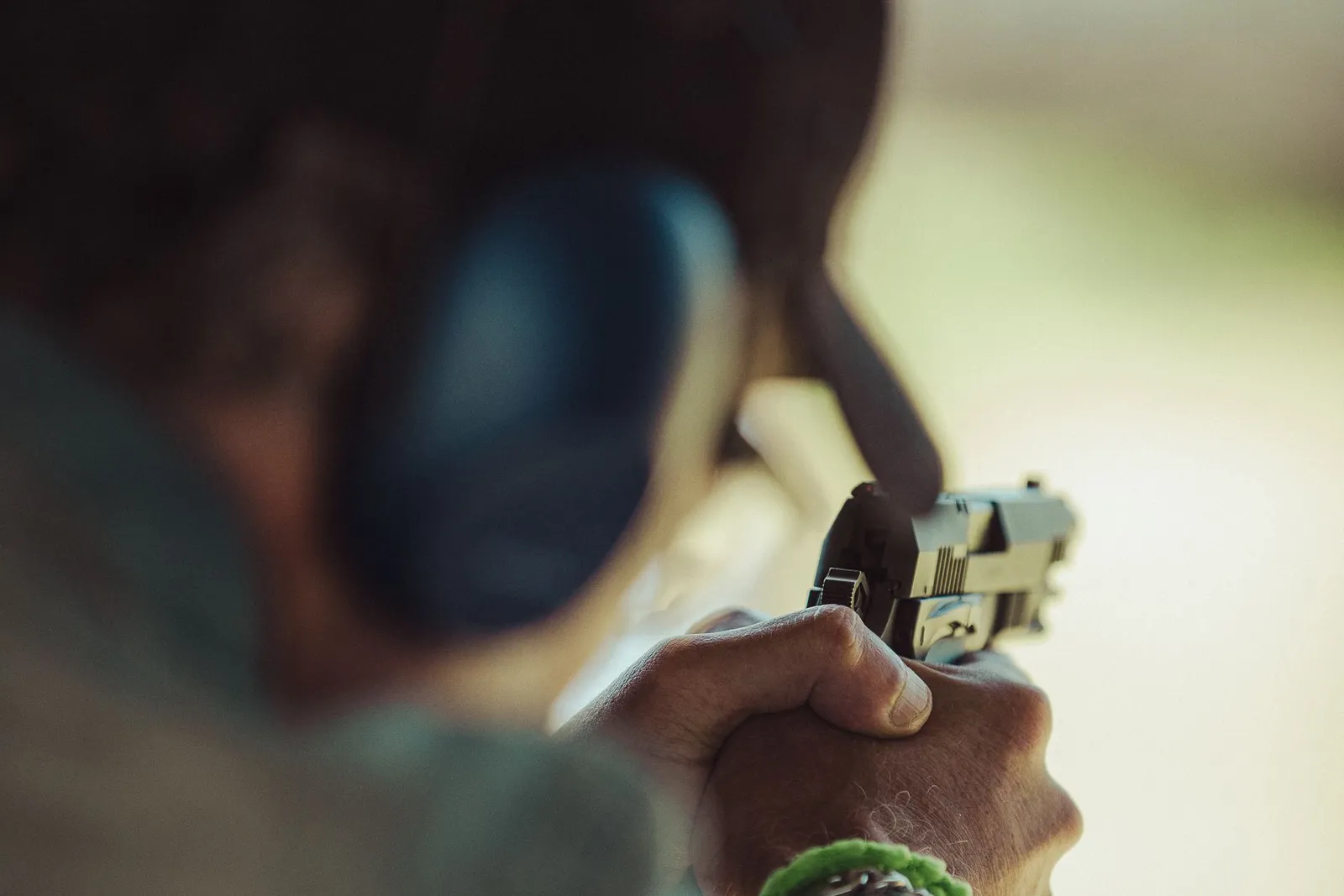Tireur au pistolet portant un casque antibruit bleu, vu de dos sur un pas de tir