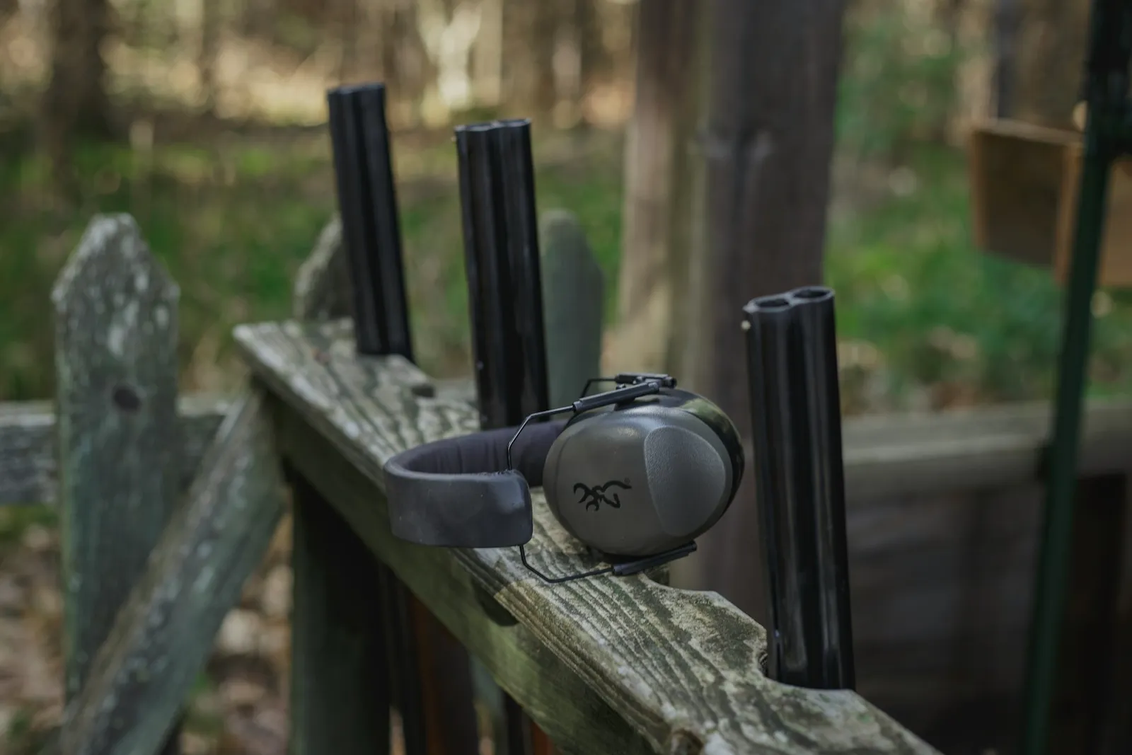 Casque antibruit posé sur une rambarde en bois à côté de supports de fusils