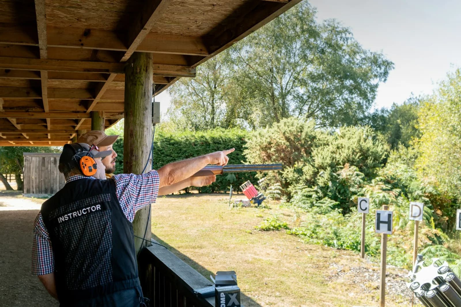 Instructeur pointant la zone de tir pour expliquer une consigne sur un pas de tir couvert