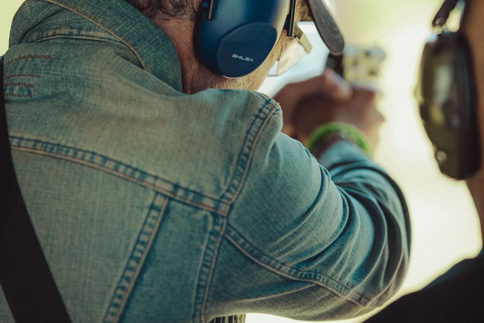 Tireur portant un casque antibruit bleu, vu de dos sur un pas de tir