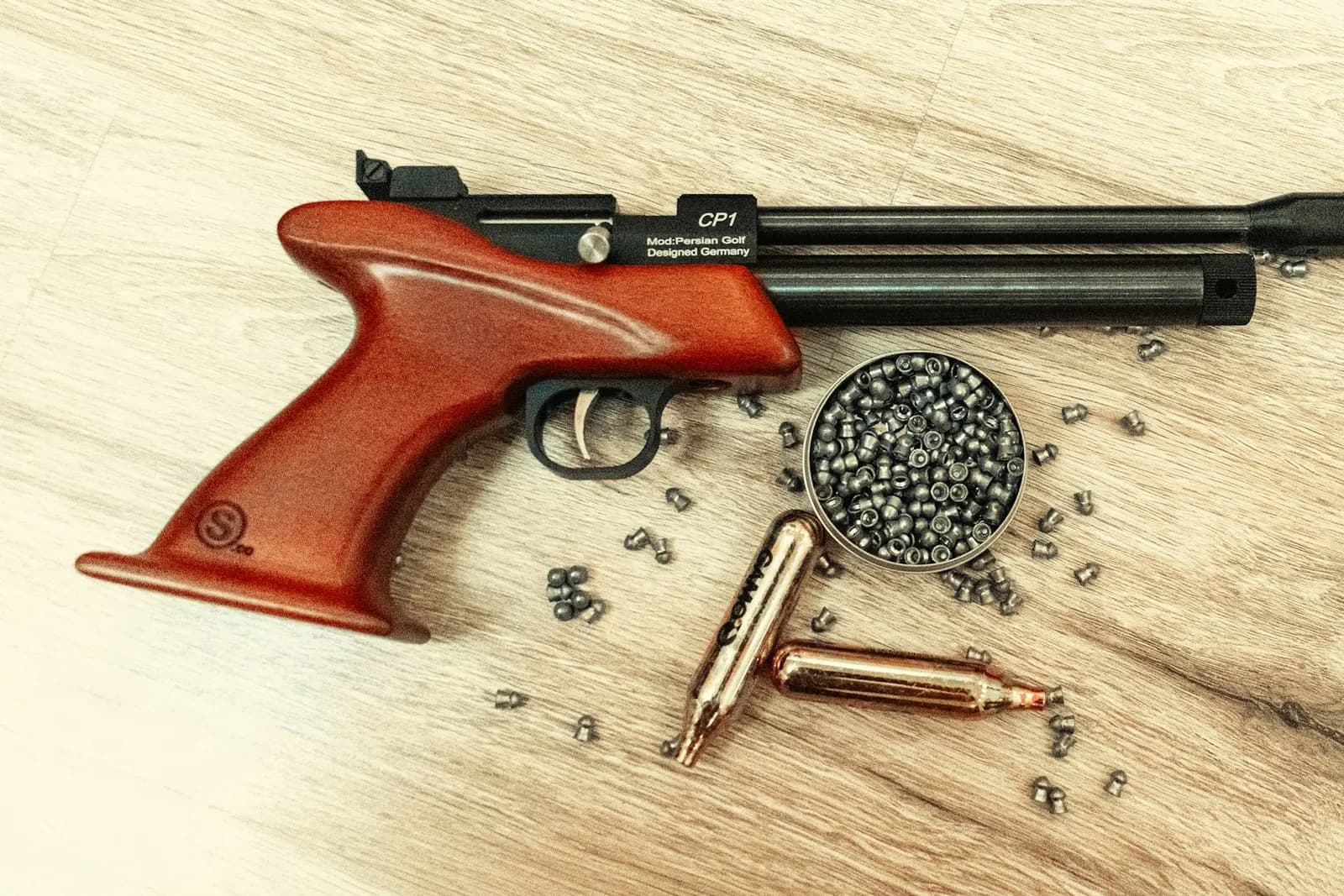 Pistolet de tir sportif à air comprimé posé sur une table en bois avec une boîte de plombs