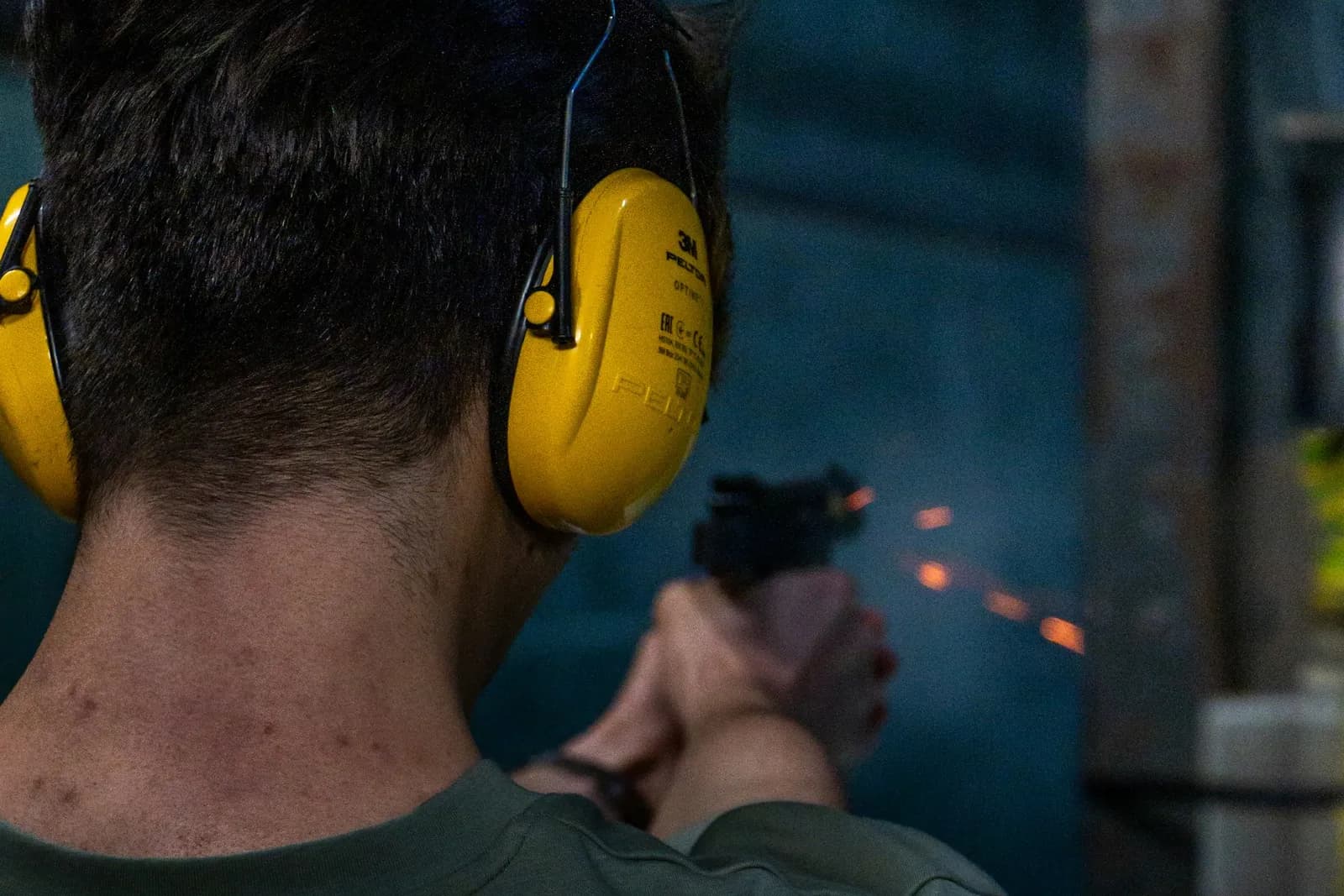 Tireur au pistolet portant un casque antibruit jaune, concentré sur son tir dans un stand