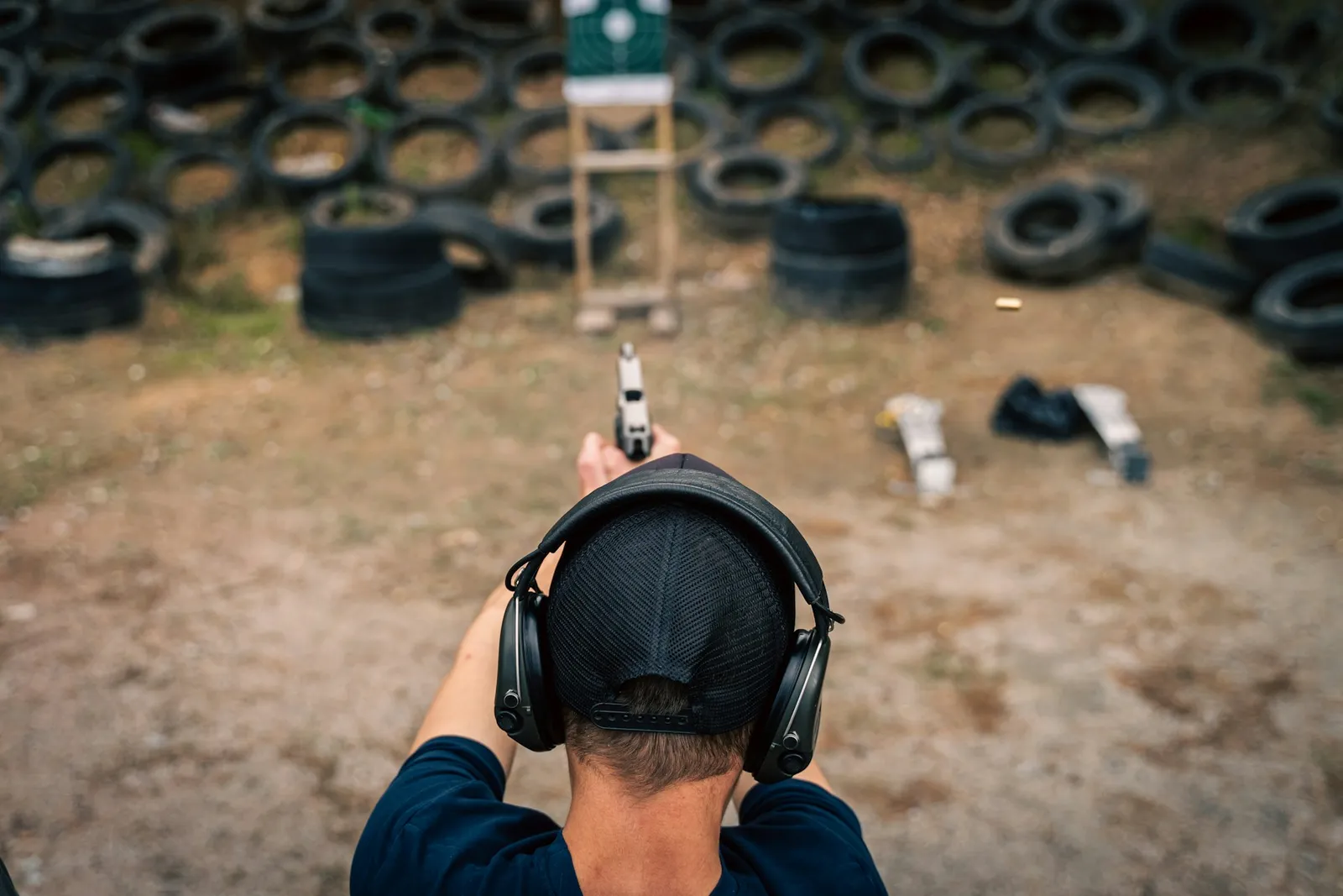 Tireur au pistolet vu de dos, casque antibruit sur la tête, visant une cible sur un pas de tir extérieur