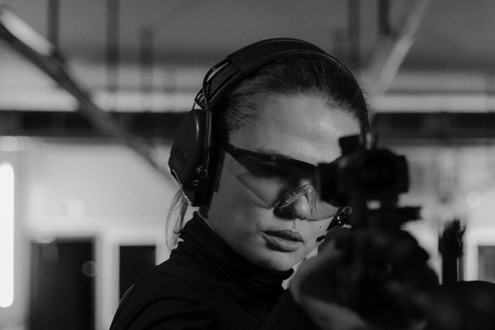 Tireuse à la carabine portant des lunettes et un casque antibruit dans un stand couvert, en noir et blanc
