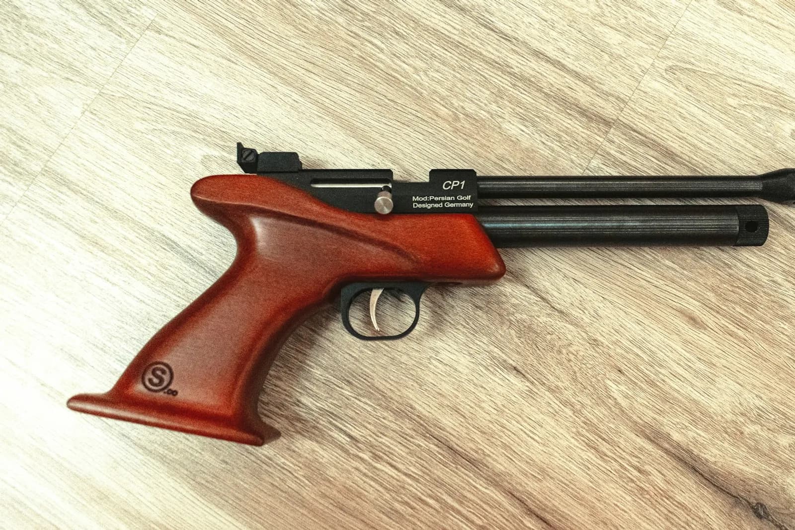 Pistolet à air comprimé à poignée en bois posé sur un plancher clair