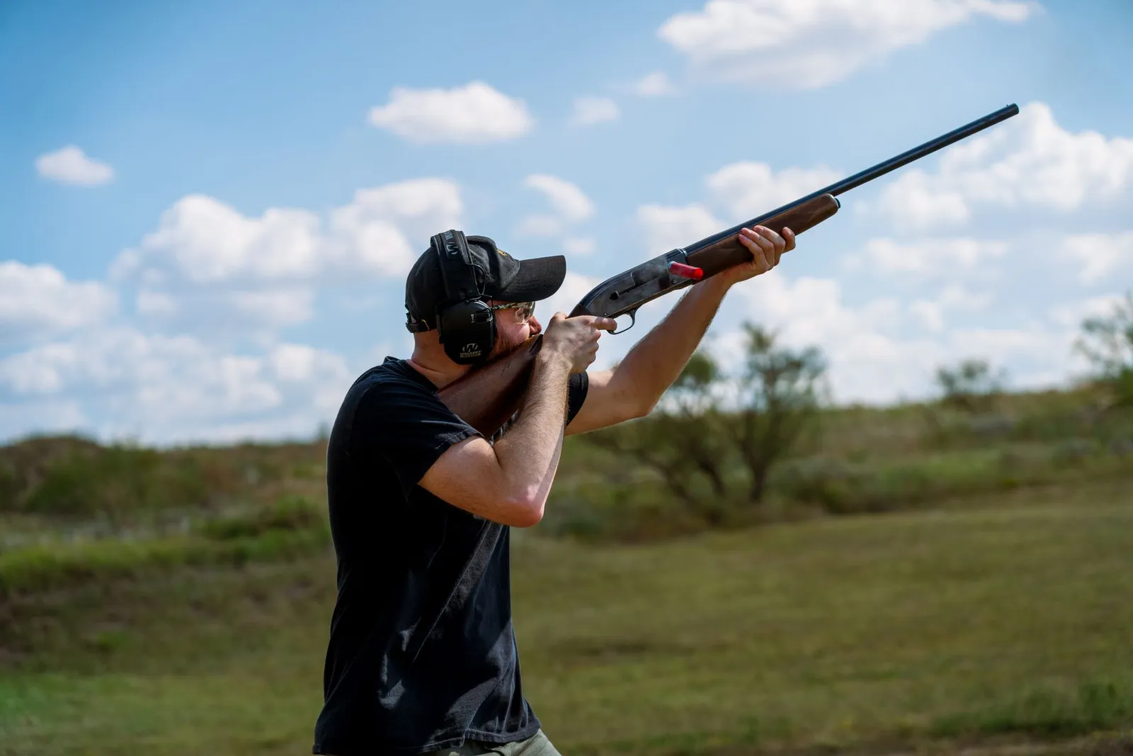 Tireur au fusil épaulant sur un terrain extérieur, casque antibruit sur les oreilles