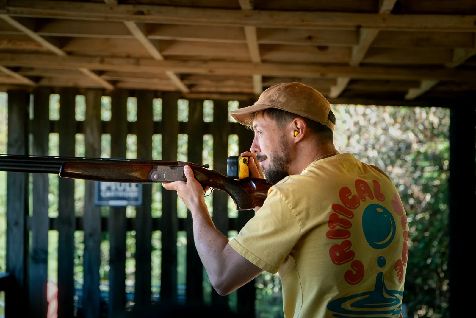 Tireur en casquette épaulant un fusil sous un abri de tir en bois